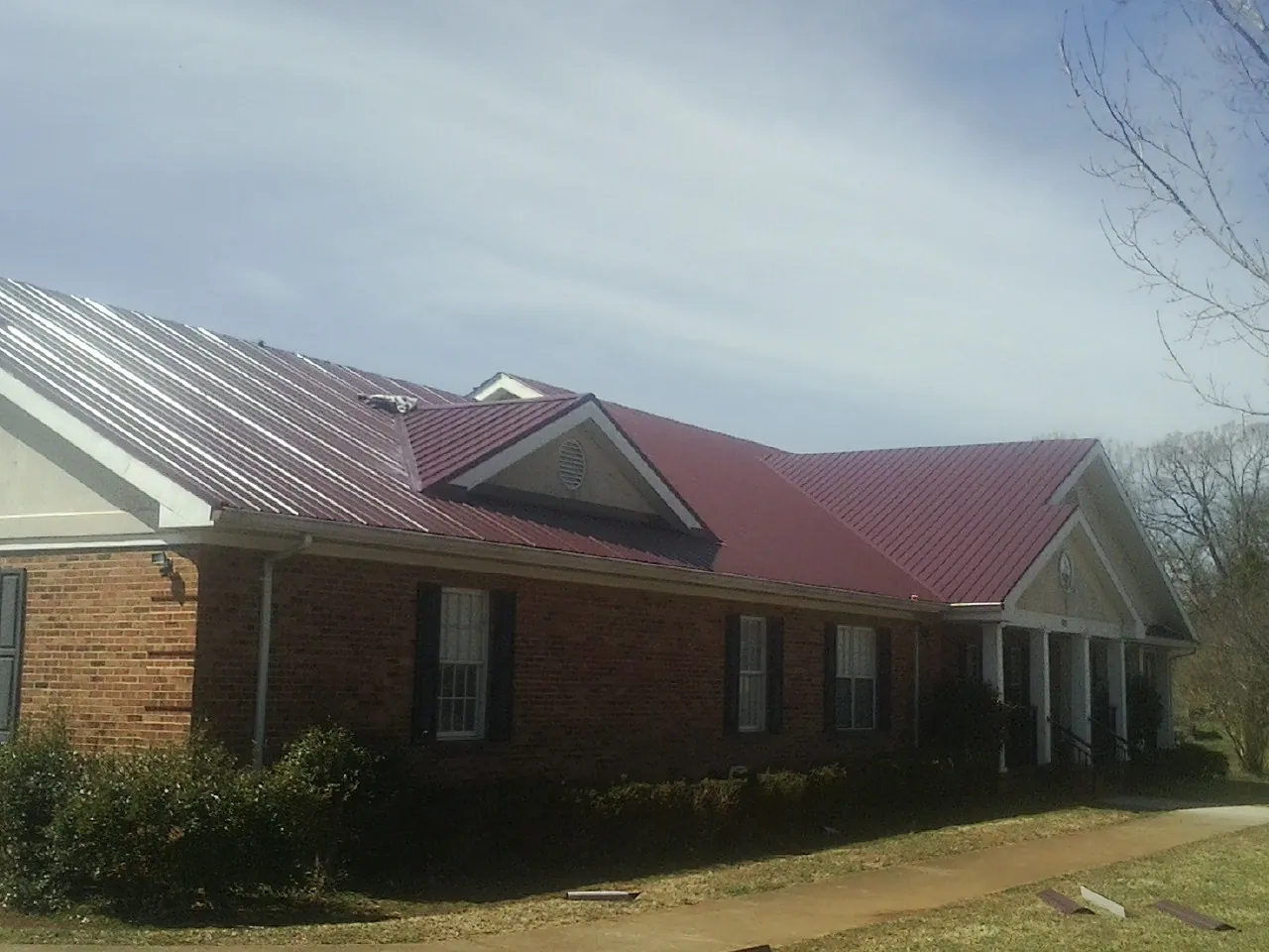 Red metal roof with gabled entries on a long brick building, from a Hail Damage Roof Repair job in Huntington