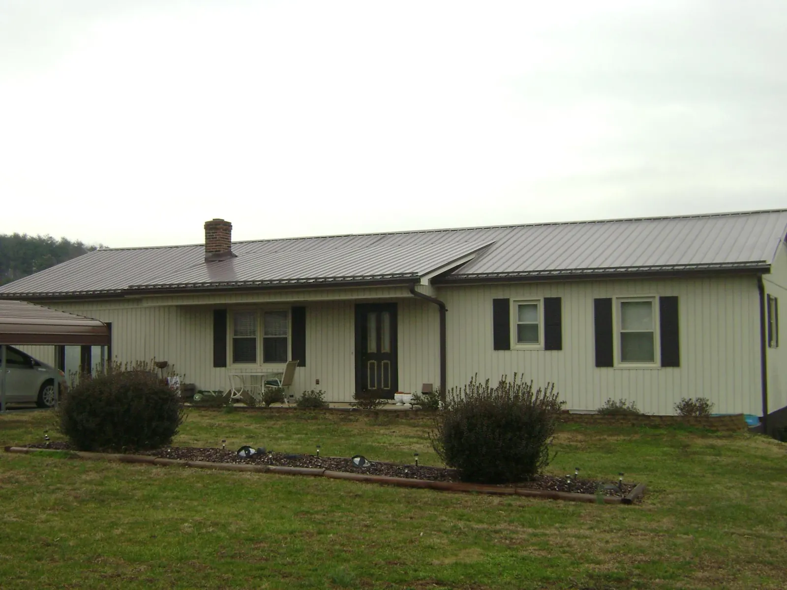 Brown metal roof on a cream sided ranch home with a brick chimney in Huntington
